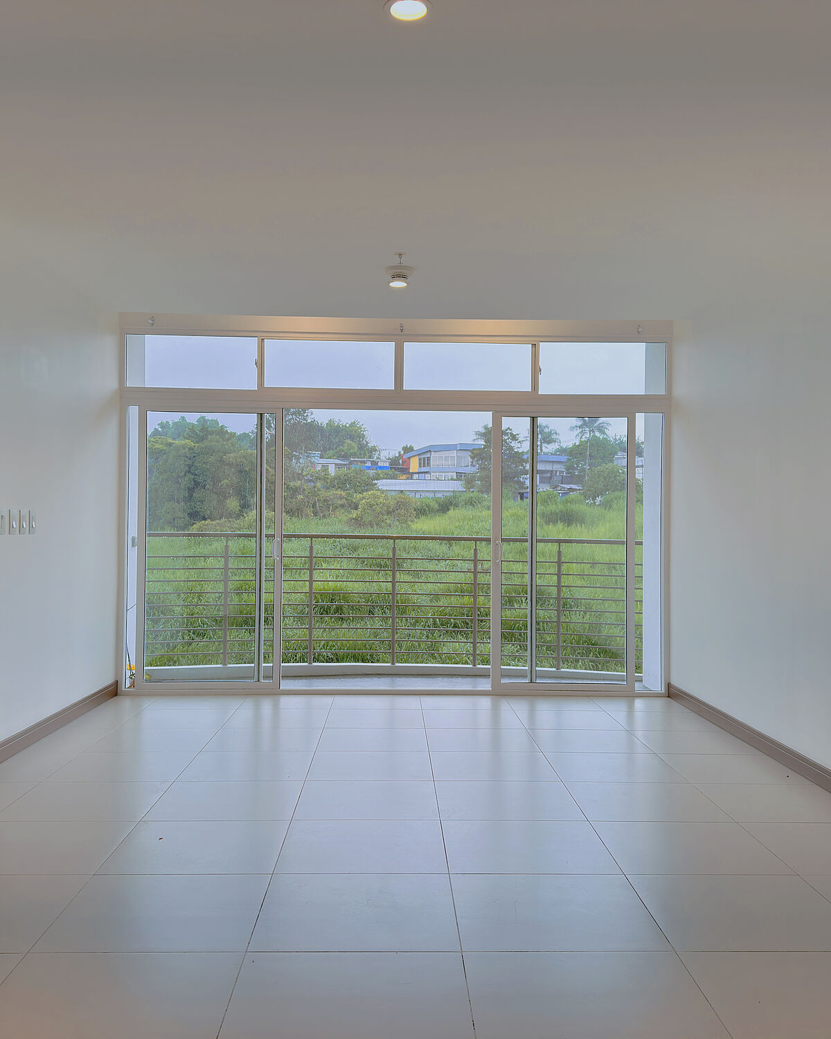 Sala vacía con ventanal de piso a techo hacia una zona verde — apartamento en Guayabos, Curridabat